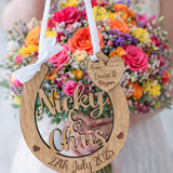 Load image into Gallery viewer, Personalised wooden wedding horseshoe with engraved names and date, held by bride in front of vibrant bridal bouquet.