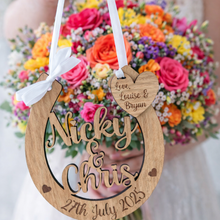 Load image into Gallery viewer, Personalised wooden wedding horseshoe with engraved names and date, held by bride in front of vibrant bridal bouquet.