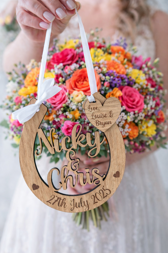 Personalised wooden wedding horseshoe with engraved names and date, held by bride in front of vibrant bridal bouquet.
