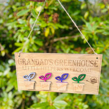 Load image into Gallery viewer, Personalised Grandadโs Greenhouse wooden sign with little helpers welcome text and plant pot design hanging in a GREEN GARDEN.