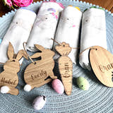 Load image into Gallery viewer, A set of four wooden hanging Easter decorations including cut-out bunny shapes and egg designs, displayed on a table with Easter eggs and fabric.