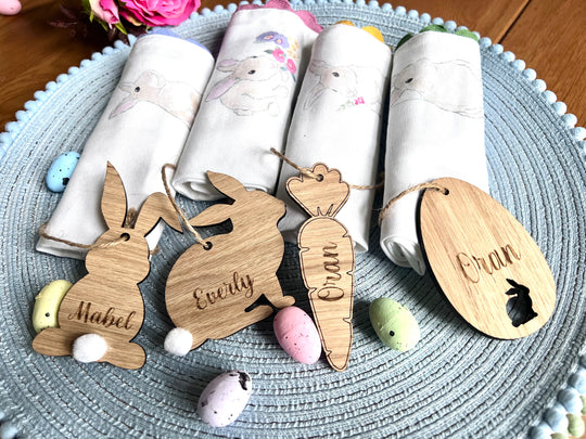 A set of four wooden hanging Easter decorations including cut-out bunny shapes and egg designs, displayed on a table with Easter eggs and fabric.