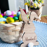 Load image into Gallery viewer, Wooden hanging bunny decoration with the name 'Mabel' inscribed, attached to a Easter tree decoration setup with colorful eggs and Easter-themed items in the background.