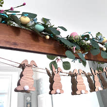 Load image into Gallery viewer, A wooden Easter Bunny Bunting hanging against a wall, featuring laser-cut bunny shapes with white pom-pom tails and decorative foliage.