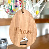 Load image into Gallery viewer, A wooden hanging decoration featuring the word 'ORLA' carved in a bunny shape, with a colorful Easter egg behind it.