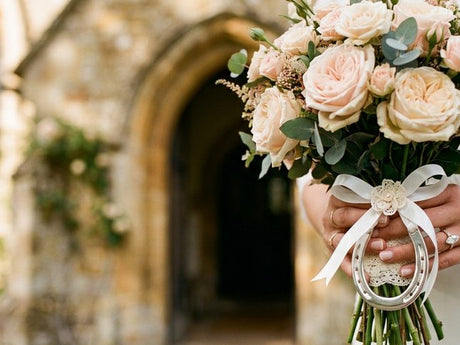 Bridal bouquet of cream and blush roses with a silver lucky horseshoe tied to the stems