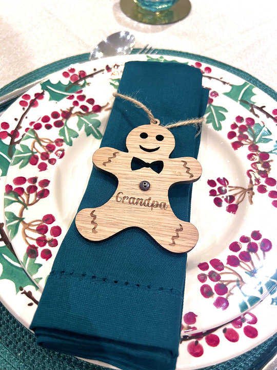 Napkin holder shaped like a gingerbread man with 'Grandpa' engraved, on a blue napkin with a decorative plate in the background.
