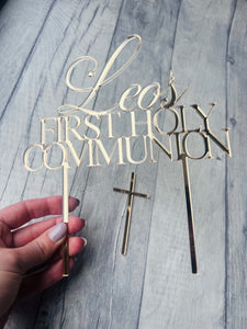 Gold 'Leo's First Holy Communion' cake topper with a cross on a wooden surface.