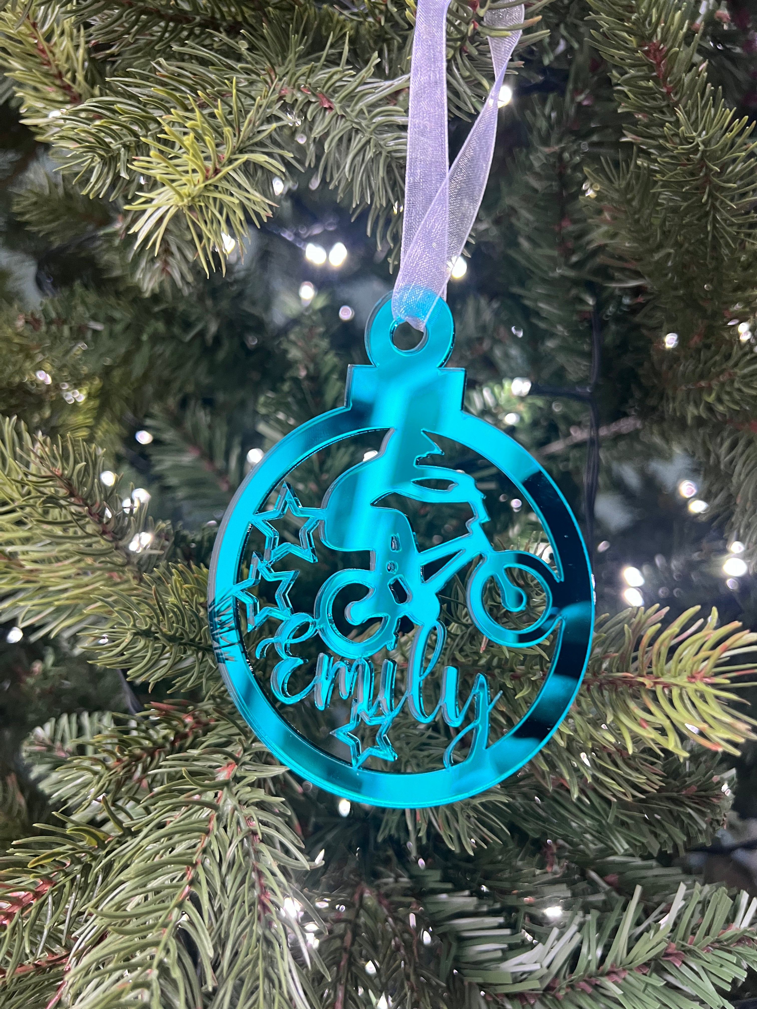 Load image into Gallery viewer, A blue mirrored acrylic Christmas tree decoration with the text 'BMX' and a star cut-out, hanging from a tree with lights and green needles in the background.
