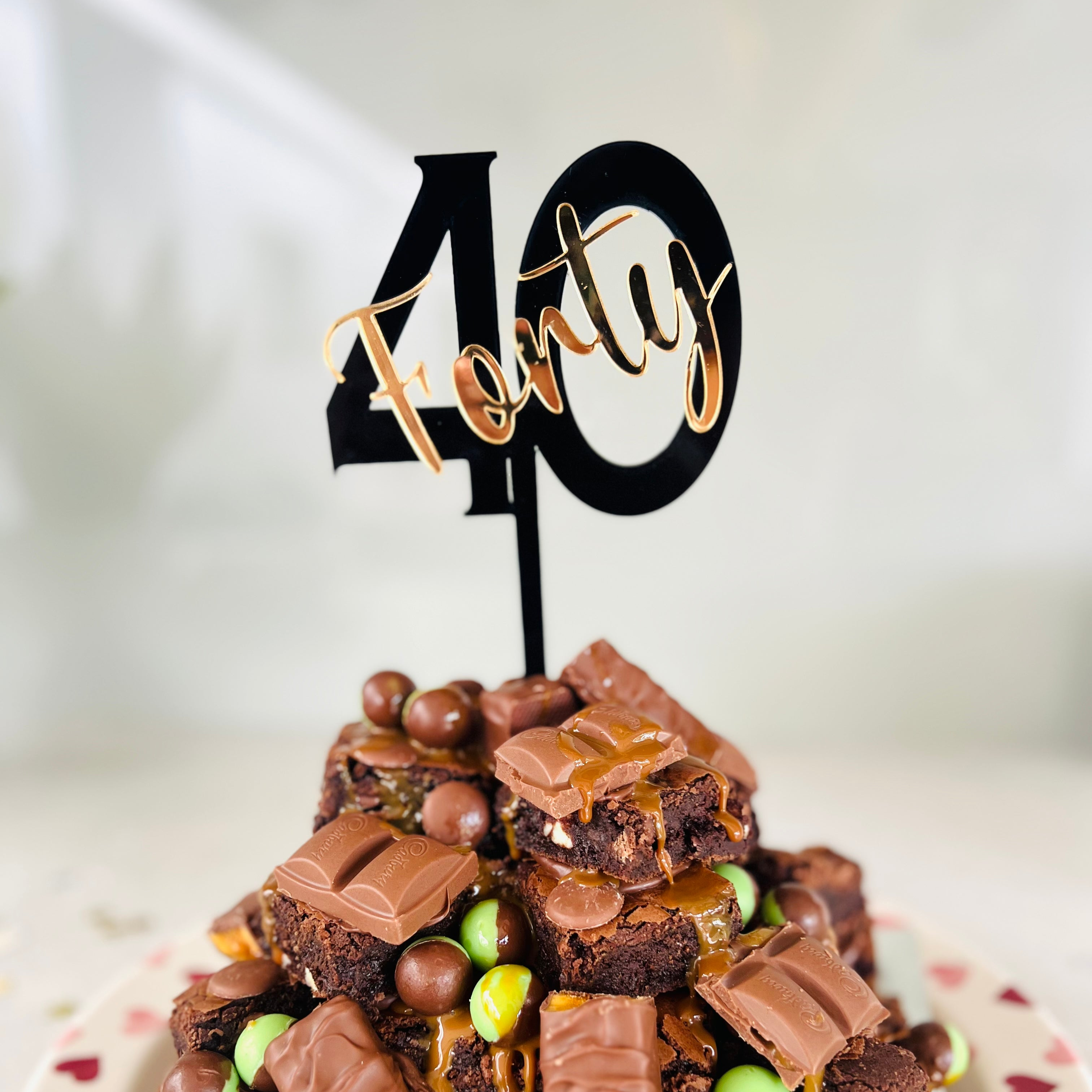 A cake topper with the number 40 in black, placed on a chocolate cake with candies.