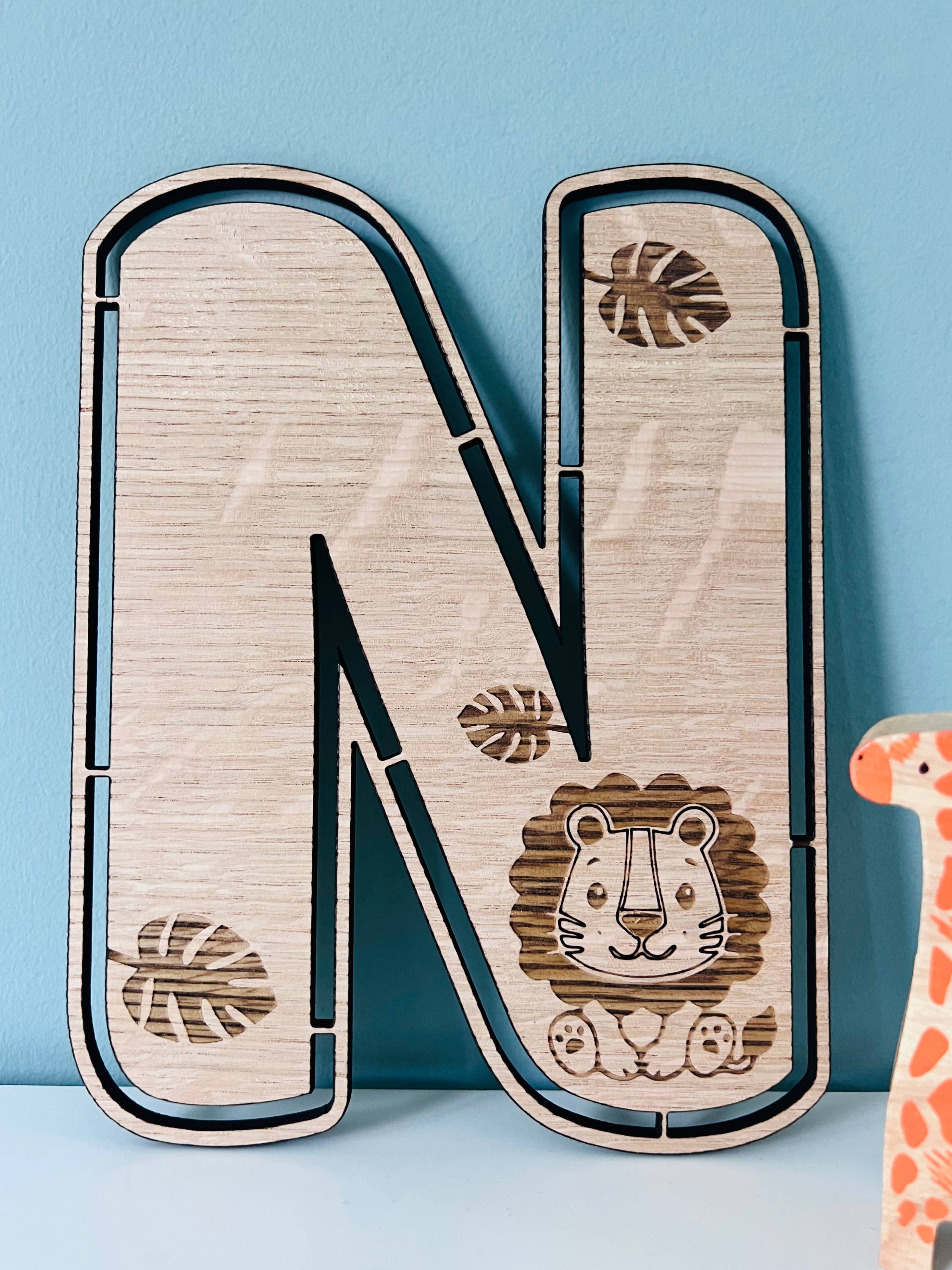 A wooden wall letter 'N' with jungle animals like a lion and giraffe illustrated on it, placed against a blue background.