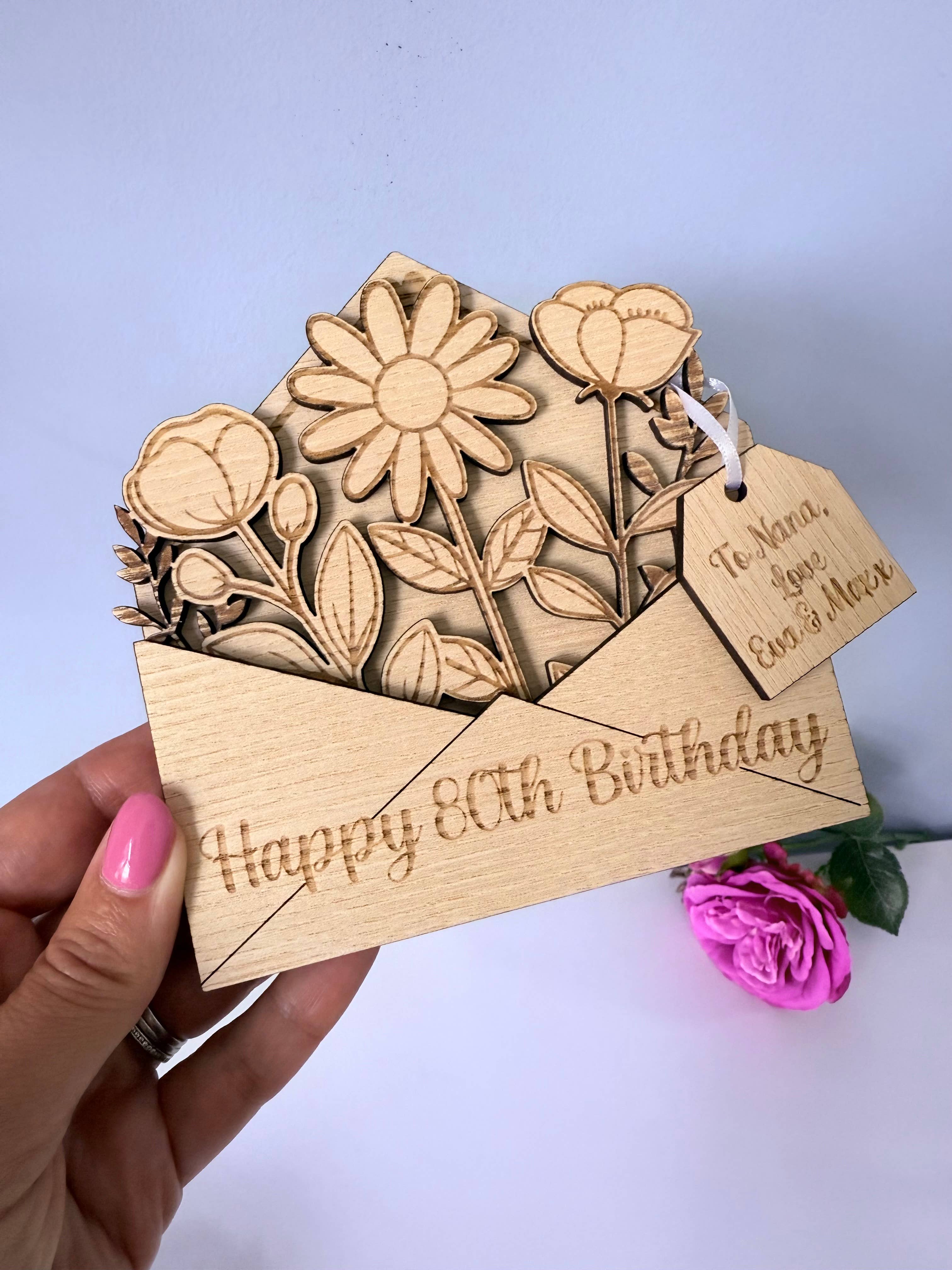 Wooden birthday card with floral design and 'Happy 80th Birthday' text, held by a hand.