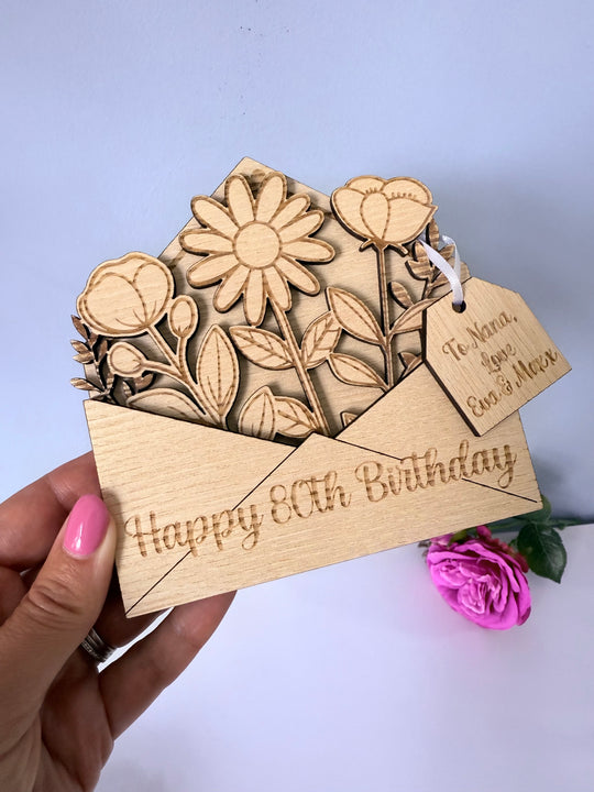 Wooden birthday card with floral design and 'Happy 80th Birthday' text, held by a hand.