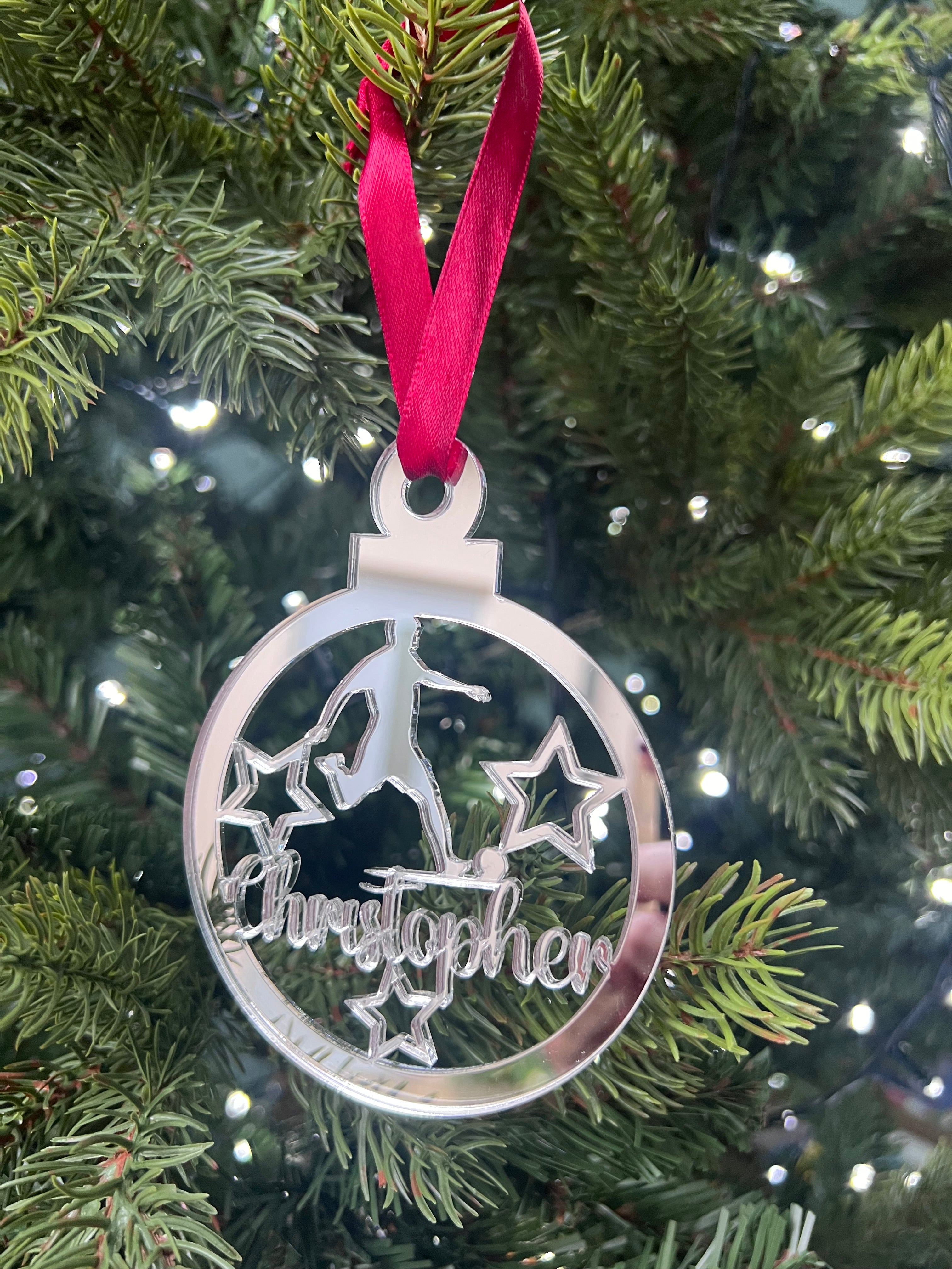 Load image into Gallery viewer, A silver-colored Christmas tree decoration featuring the name 'Christopher' laser cut and engraved on a round mirrored acrylic ornament, with a red ribbon hanging from the top.
