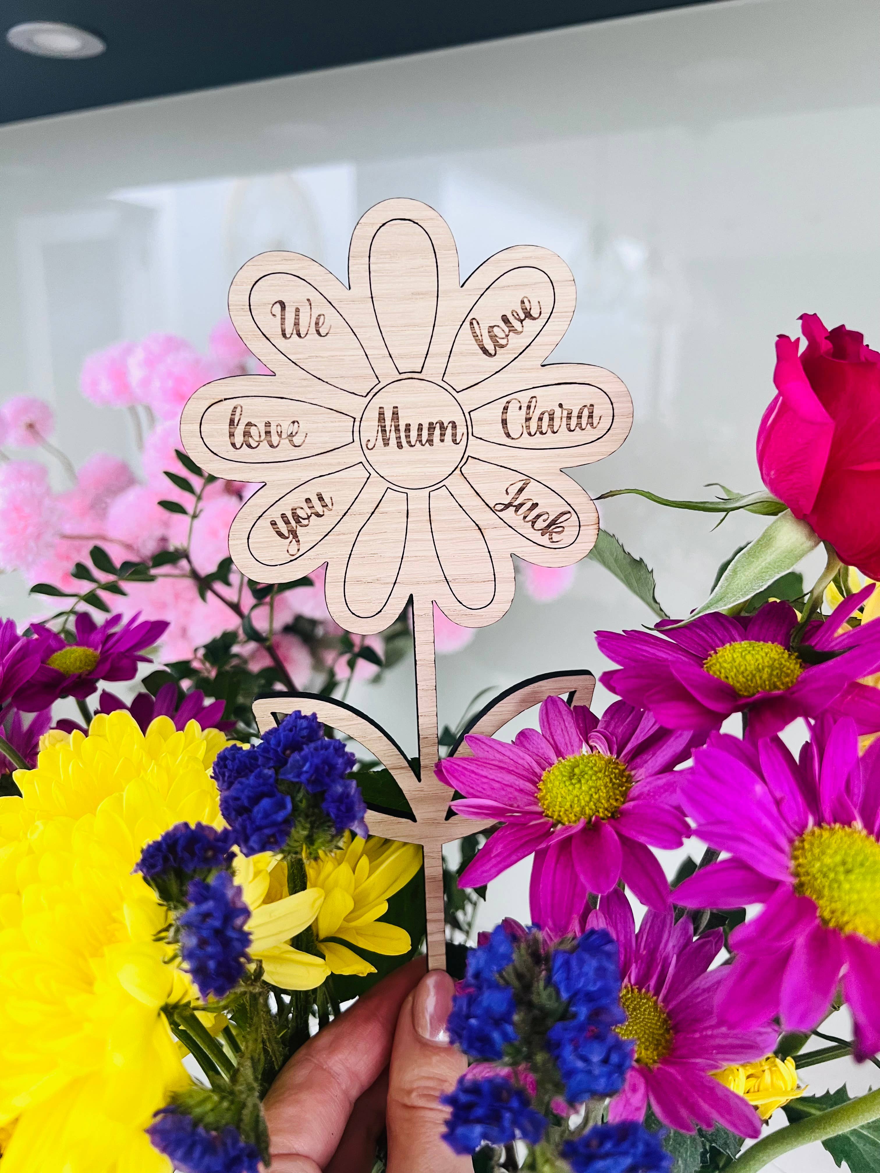 A freestanding wooden flower-shaped card with personalized message, placed amidst vibrant flowers.