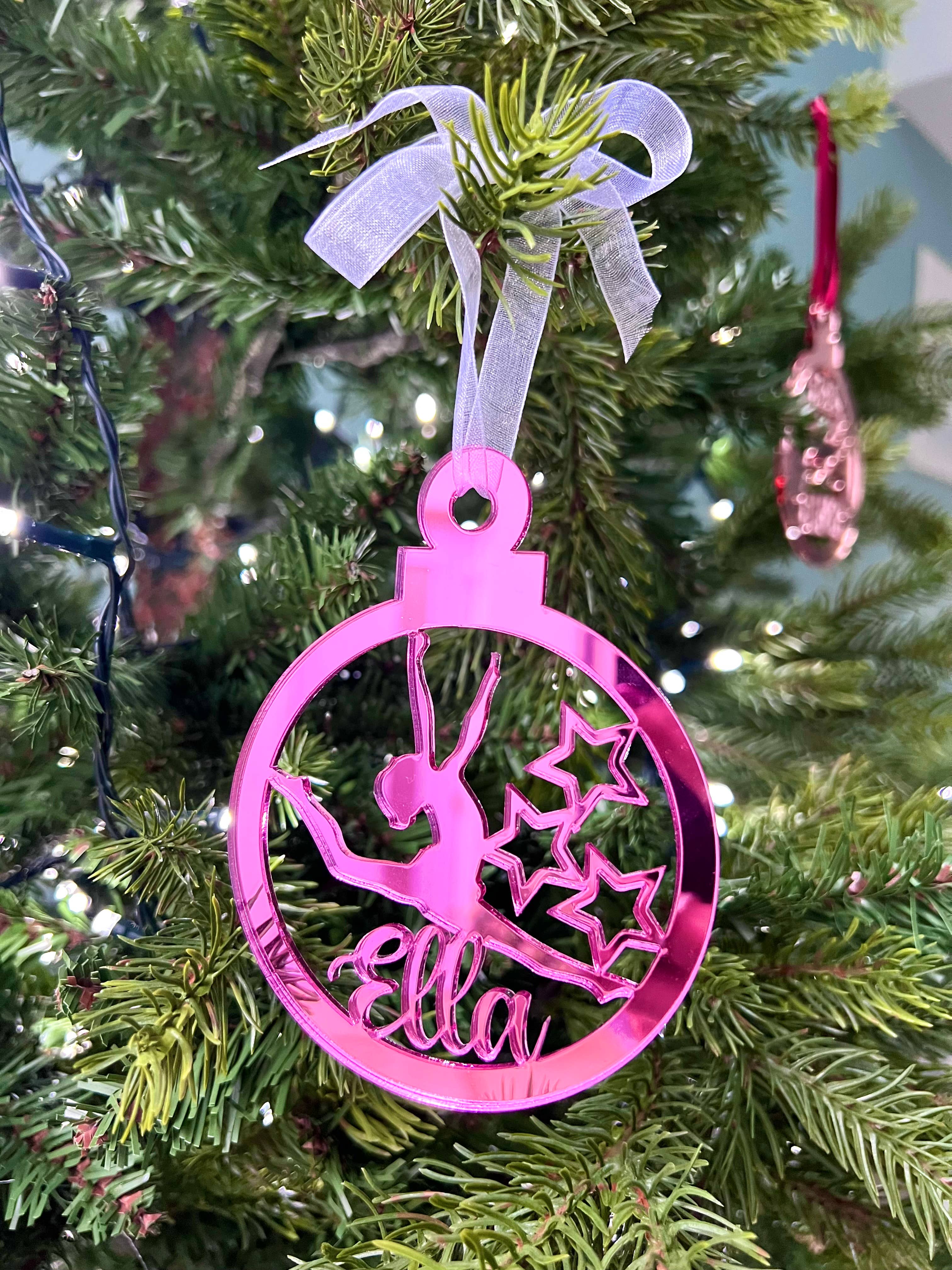 A pink circular Christmas tree decoration with a gymnast figure in the center, hanging on a Christmas tree.