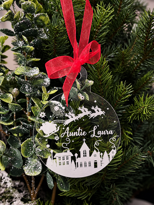 Personalised clear acrylic Christmas bauble with Santa, reindeer, snowy village, stars and the name Auntie Laura