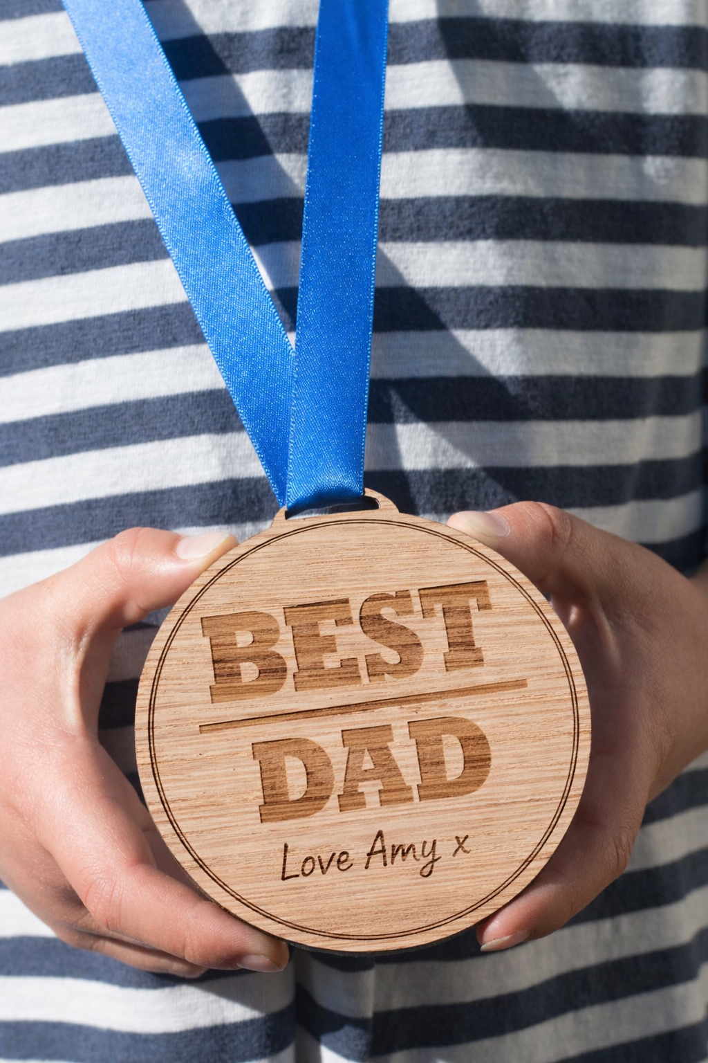 Best dad wooden medal Fathers Day gift held by Dad with blue ribbon and gift background UK