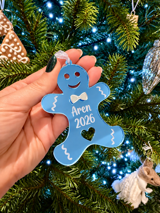 Personalised blue acrylic gingerbread Christmas ornament engraved with Aren 2026 on a Christmas tree