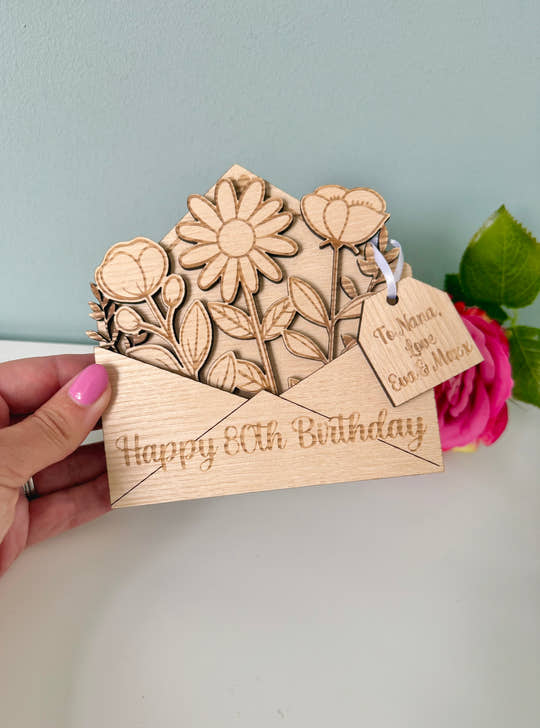 Wooden birthday card with floral design and 'Happy 80th Birthday' text, held by a hand.