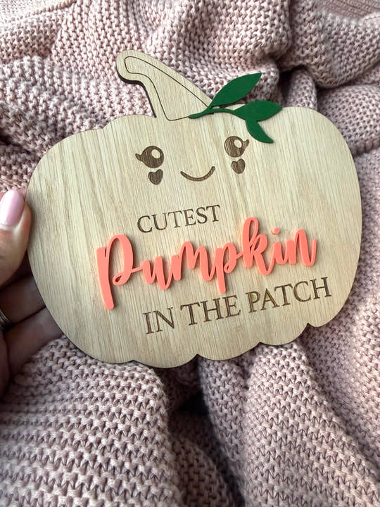 Wooden pumpkin-shaped sign with 'Cutest Pumpkin in the Patch' text on a textured fabric background