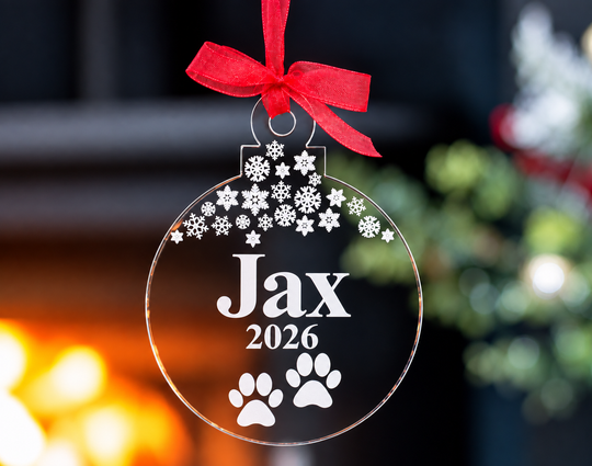 Personalised dog Christmas bauble featuring the name Jax, 2026, paw prints and snowflakes on clear acrylic with a red ribbon