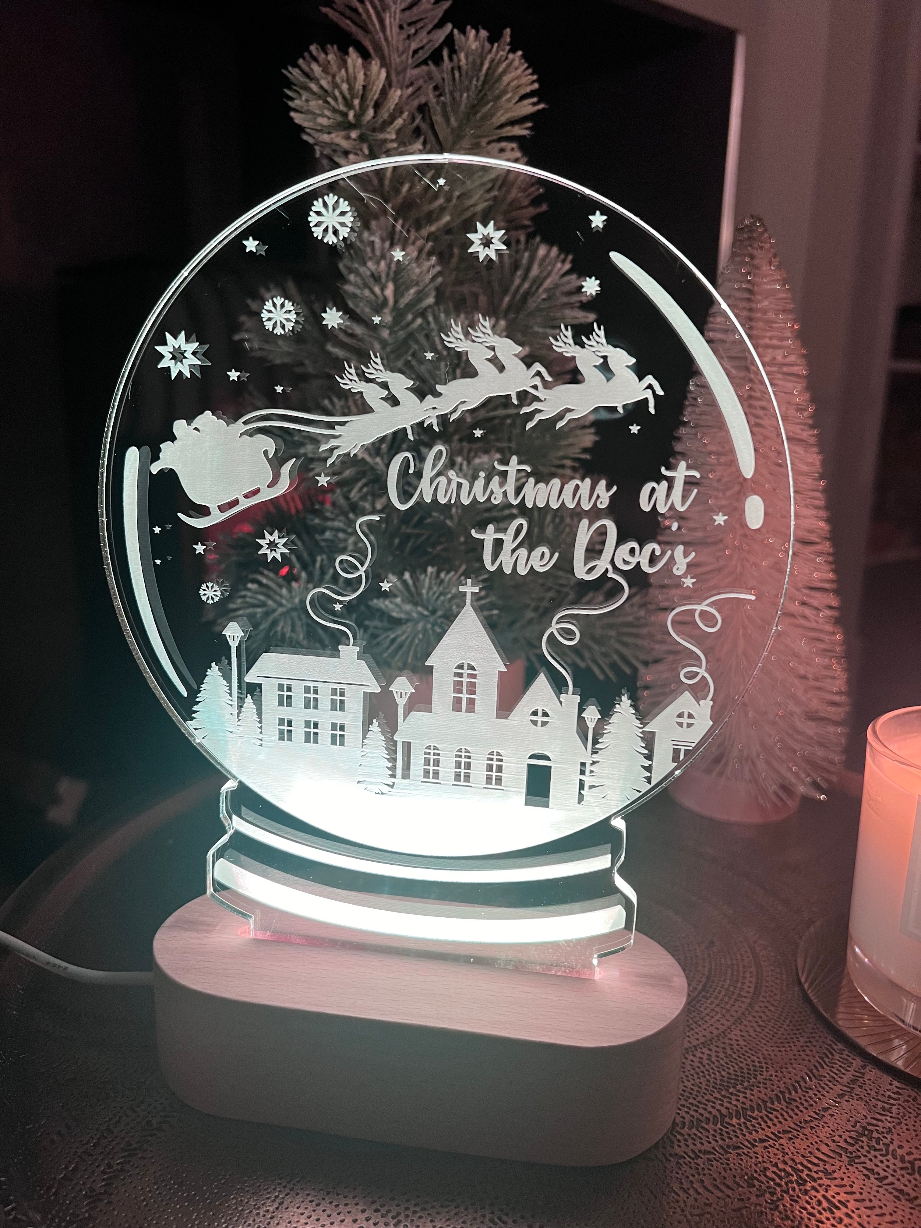 Load image into Gallery viewer, A clear acrylic Christmas snowglobe with a laser cut and engraved design featuring a reindeer, house, and Christmas tree, with a personalized text 'Christmas at the Door'.
