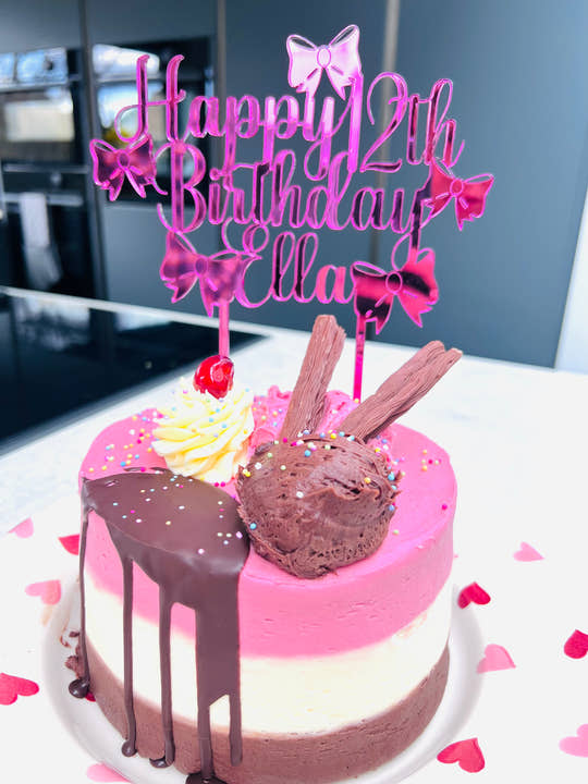 Pink mirrored acrylic personalised cake topper reading “Happy 12th Birthday Ella” displayed on a ice cream drip otake with flakes