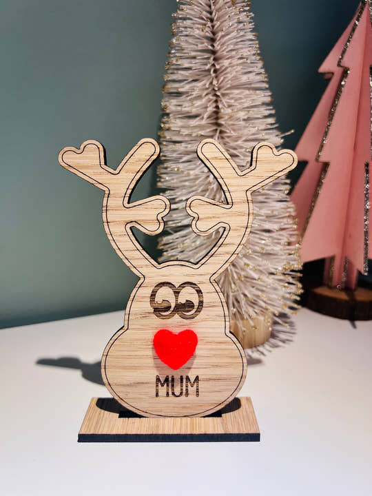 Wooden reindeer place name holder with red nose and engraved name “Mum” on a festive Christmas dinner table with holly plates and holiday decorations.