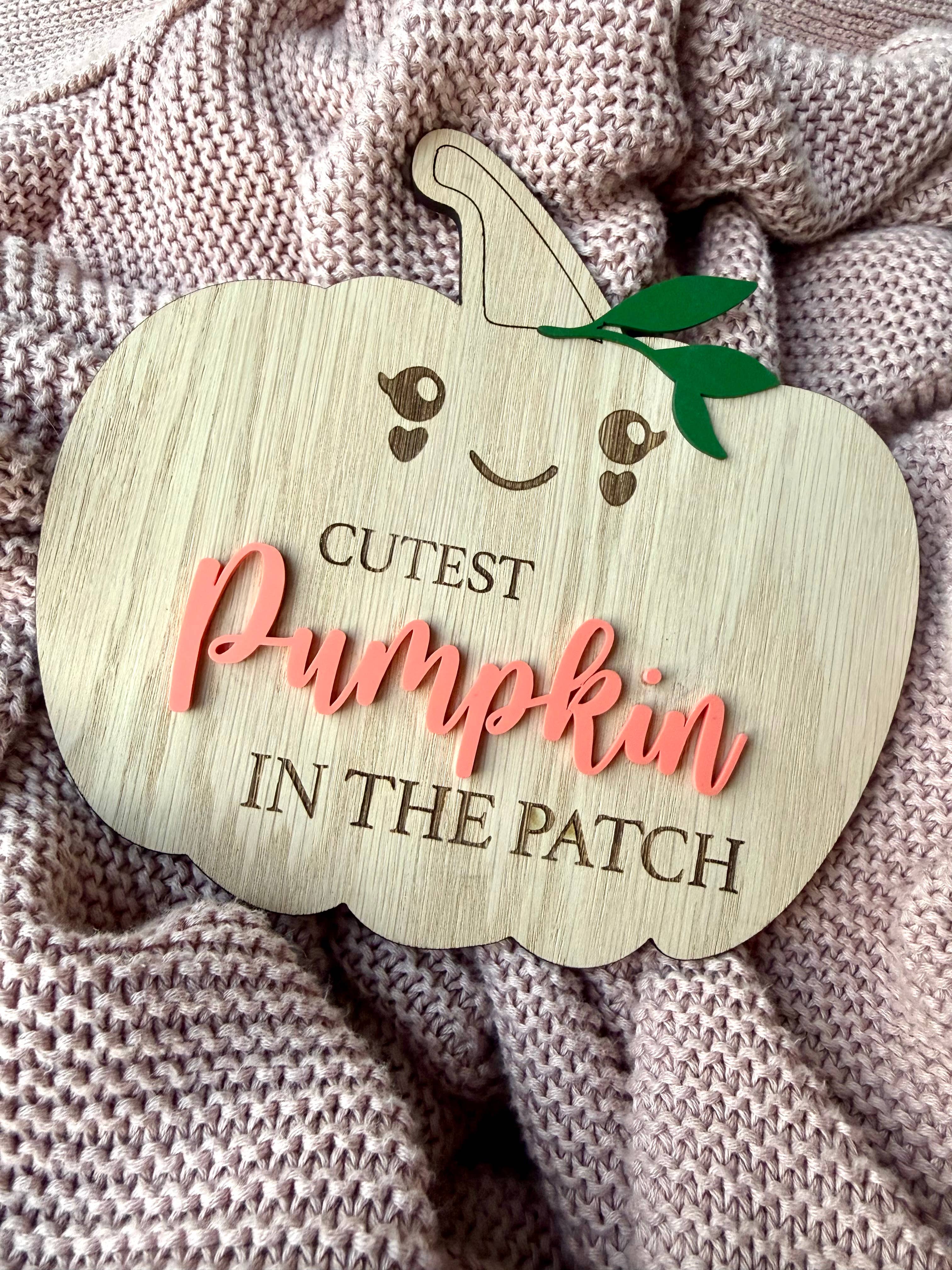 Wooden pumpkin-shaped sign with 'Cutest Pumpkin in the Patch' text on a textured fabric background