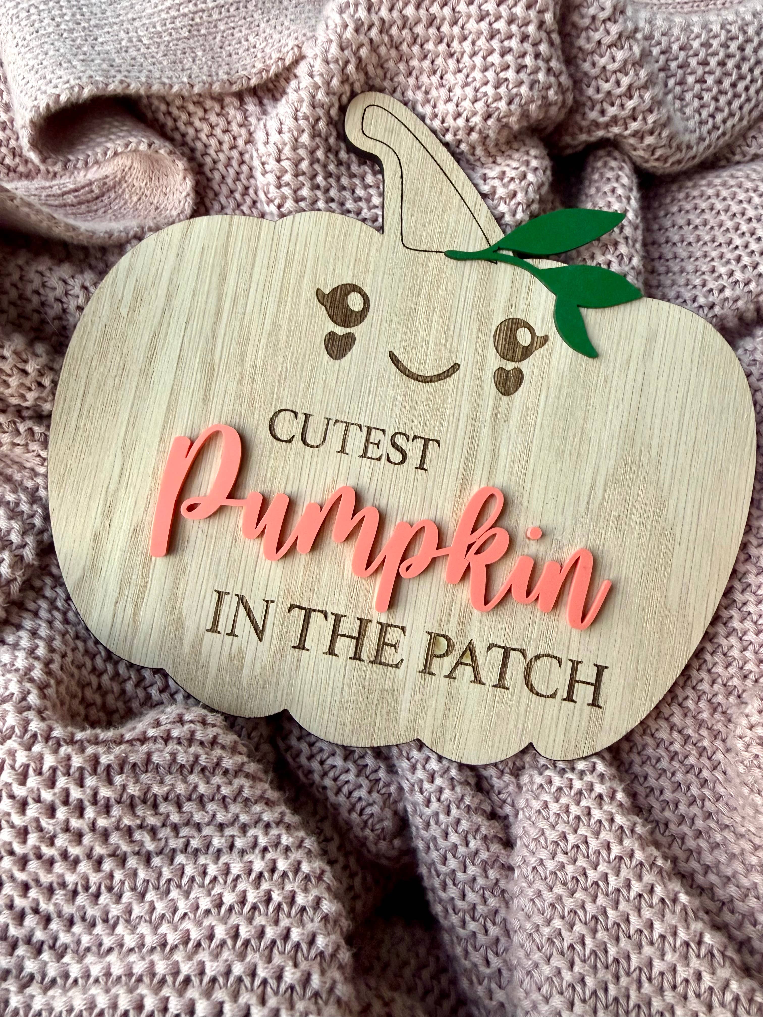 Wooden pumpkin-shaped sign with 'Cutest Pumpkin in the Patch' text on a textured fabric background