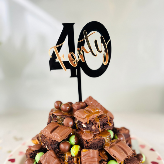 A cake topper with the number 40 in black, placed on a chocolate cake with candies.