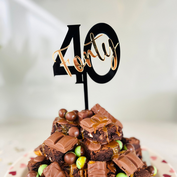 A cake topper with the number 40 in black, placed on a chocolate cake with candies.