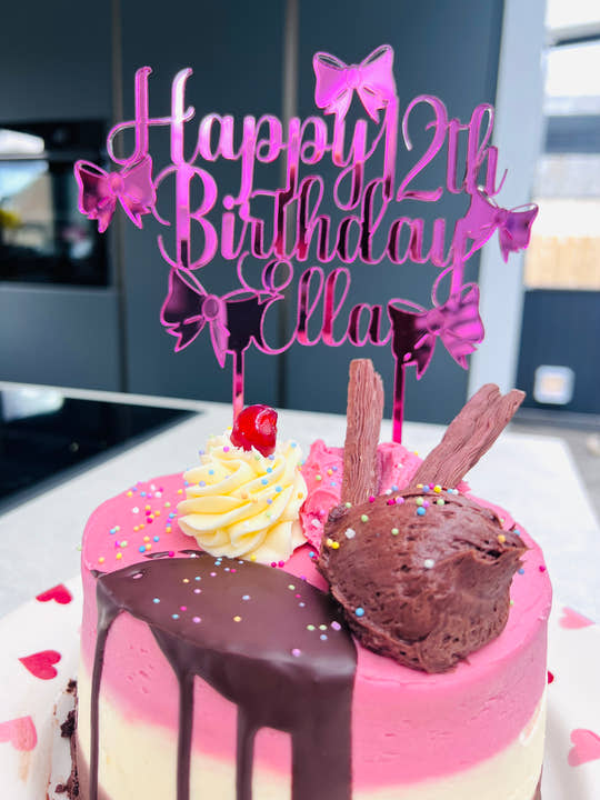 Pink mirrored acrylic personalised cake topper reading “Happy 12th Birthday Ella” displayed on a ice cream drip otake with flakes