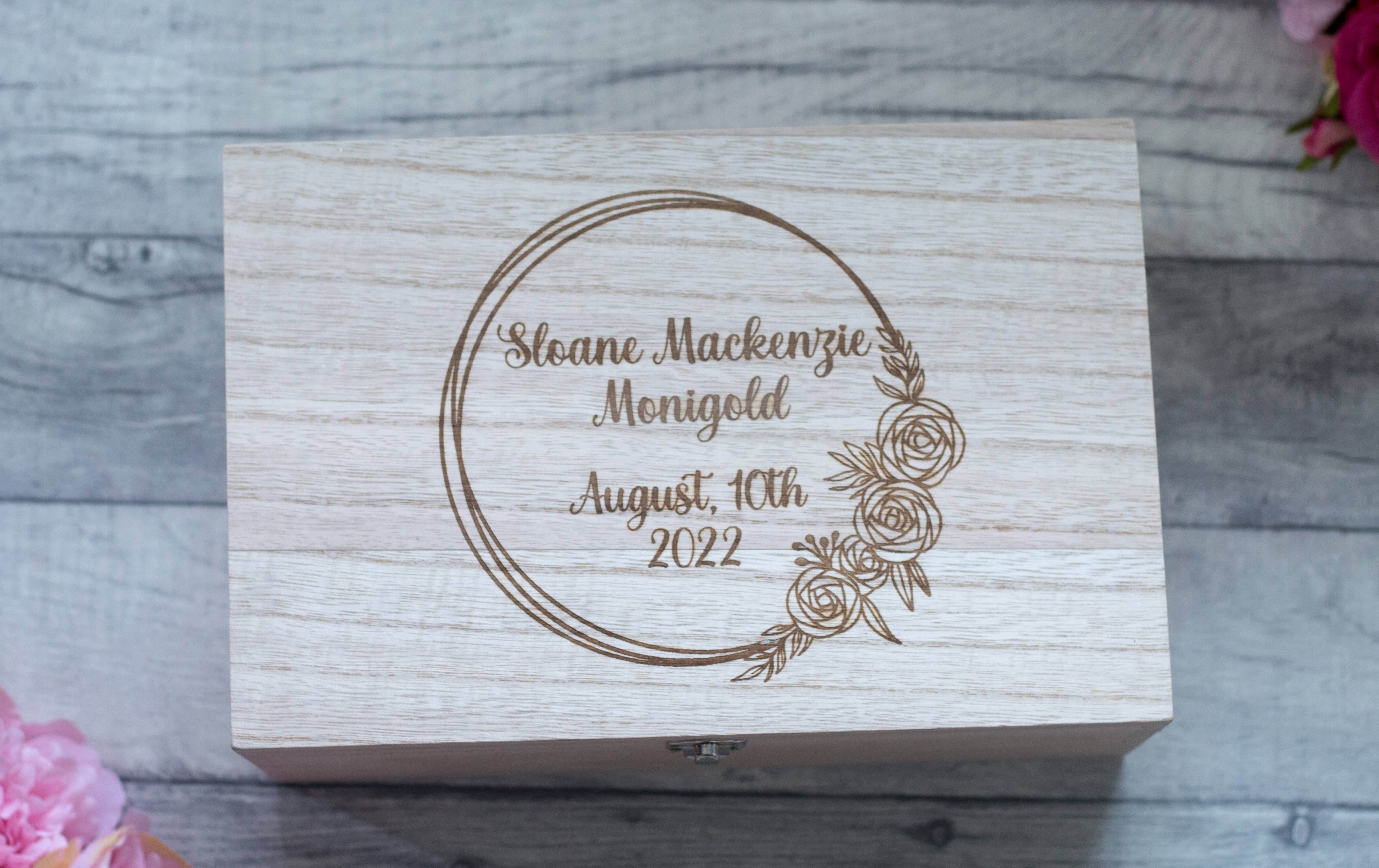 A wooden baby memory box with a brass effect latch, engraved with a floral design and text.