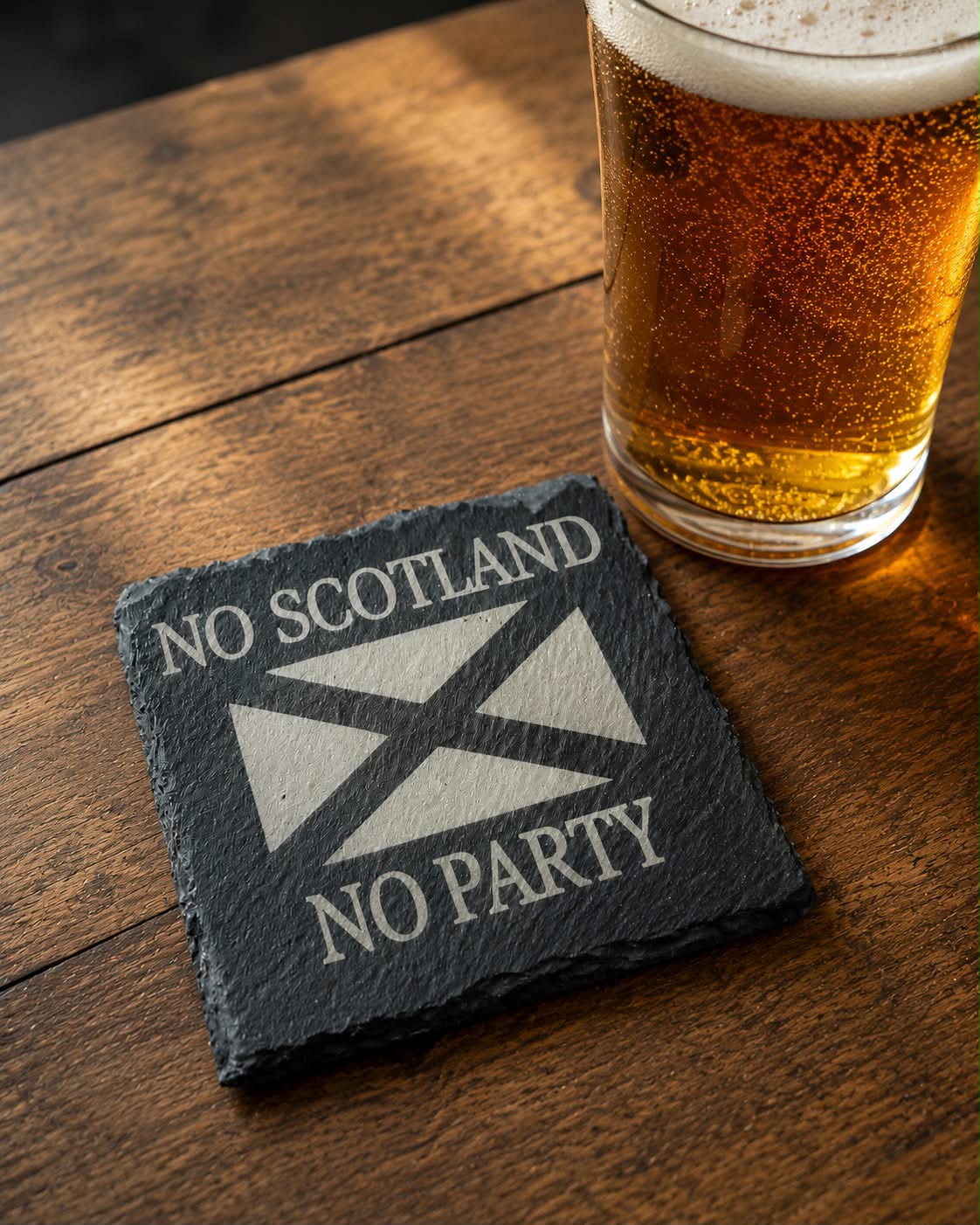 Slate coaster with Scottish flag design and 'No Scotland, No Party' text on a wooden surface with a glass of beer.