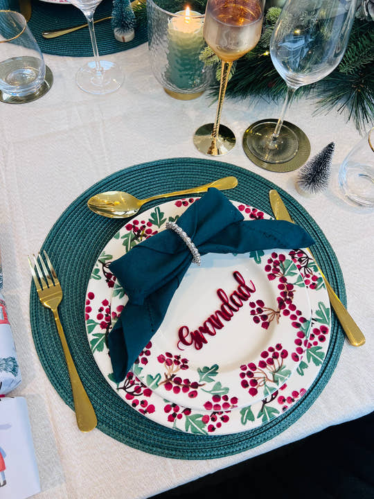 Christmas dinner table setting with personalised acrylic place name ‘Grandad’ in red, festive plate and green napkin
