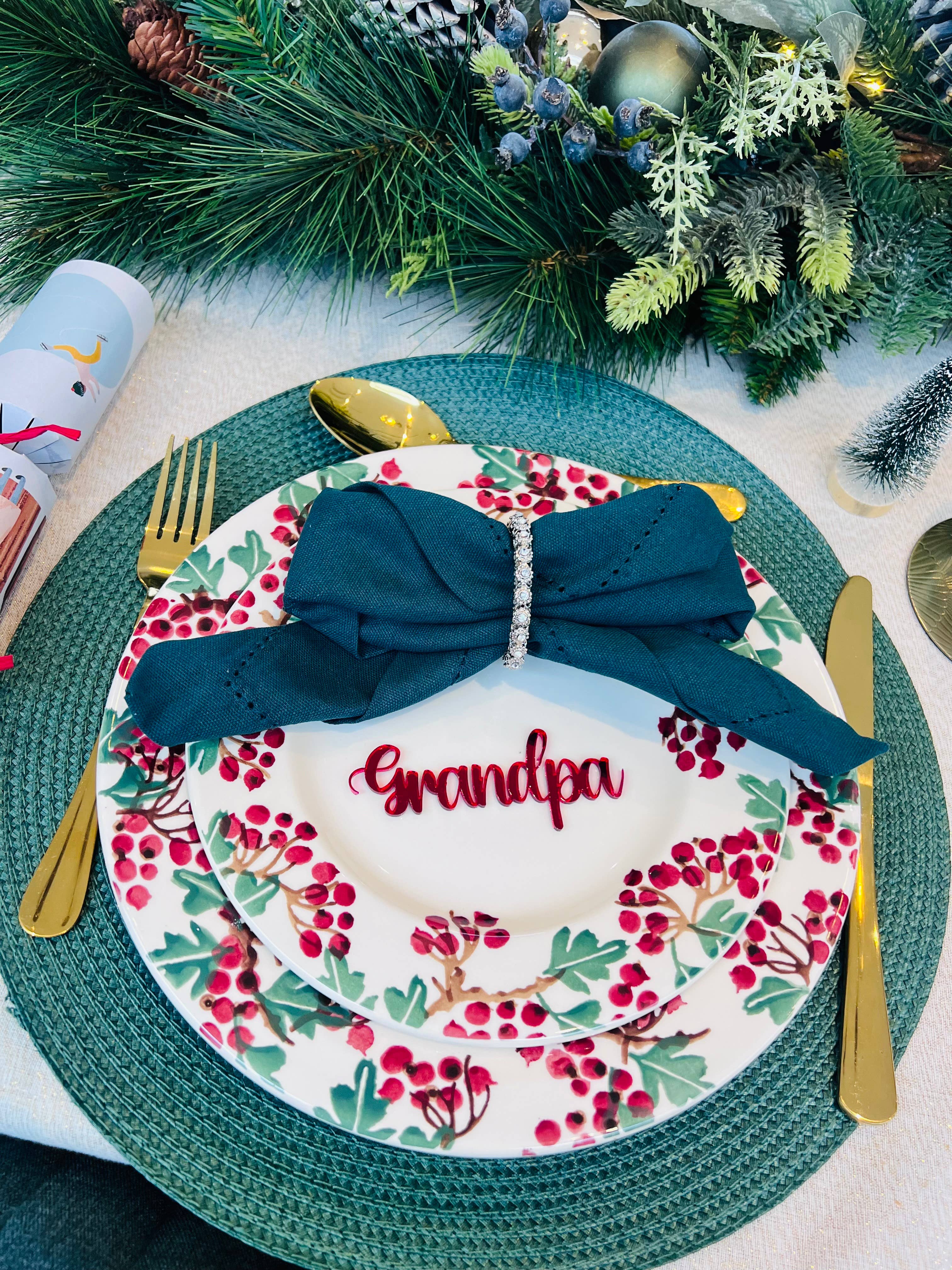Christmas dinner table setting with personalised acrylic place name ‘Grandpa’ in red, festive plate and green napkin