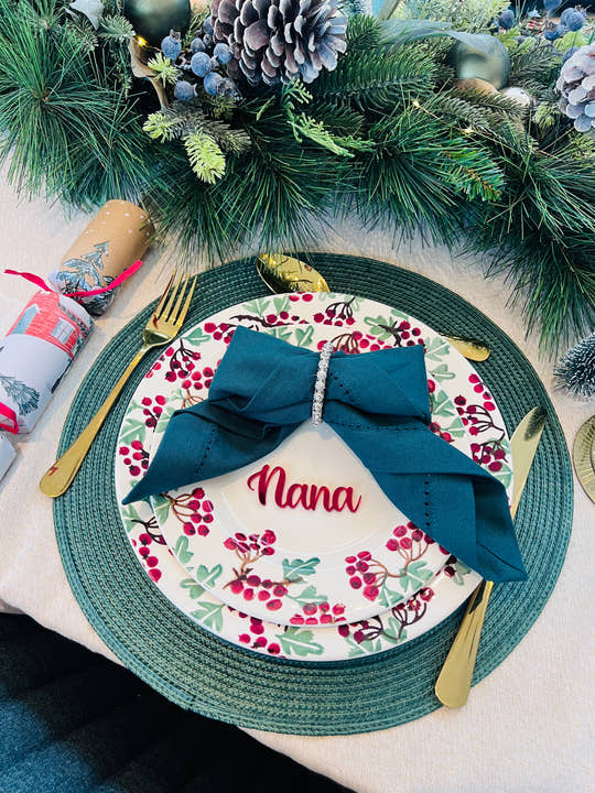 Christmas dinner table setting with personalised acrylic place name ‘Nana’ in red, festive plate and green napkin