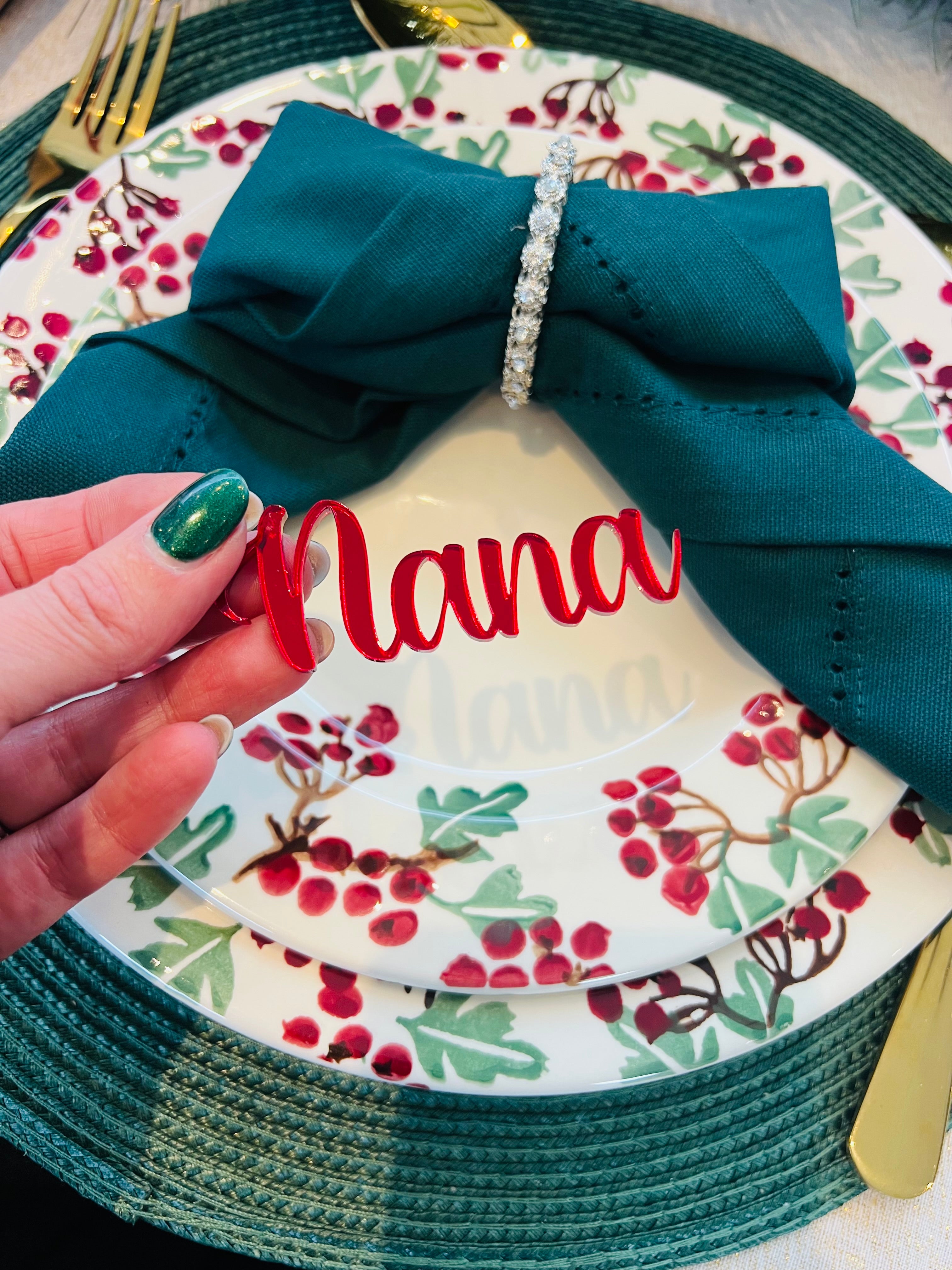 Load image into Gallery viewer, Hand holding personalised red acrylic place name ‘Nana’ on Christmas dinner plate with holly berry design
