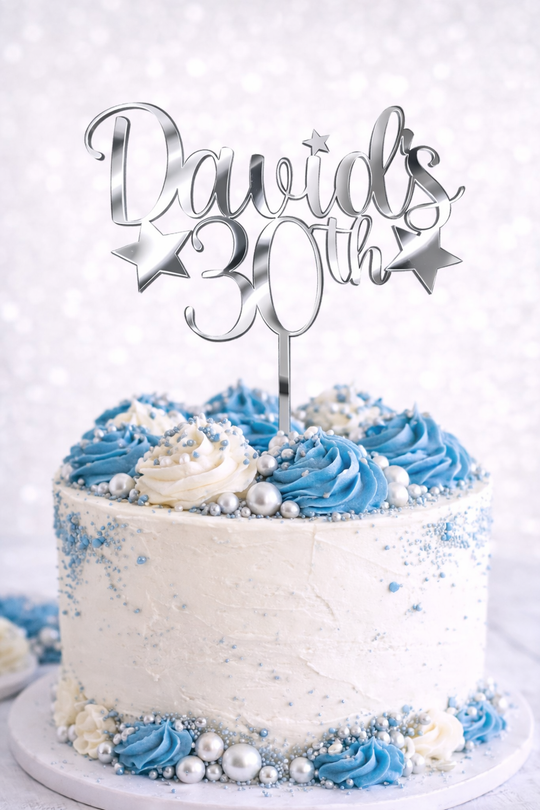 Personalised silver mirror acrylic birthday cake topper with custom name and age on white celebration cake with blue buttercream and silver decorations.