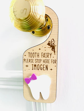 Personalised wooden Tooth Fairy door hanger with engraved text and white tooth shape with purple bow, hanging on a brass doorknob