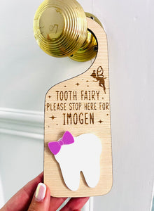 Personalised wooden Tooth Fairy door hanger with engraved text and white tooth shape with purple bow, hanging on a brass doorknob