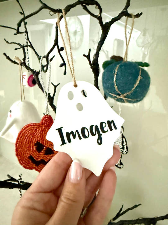 Personalised ghost Halloween tree decoration with engraved name hanging on a Halloween tree with pumpkins and spooky ornaments.