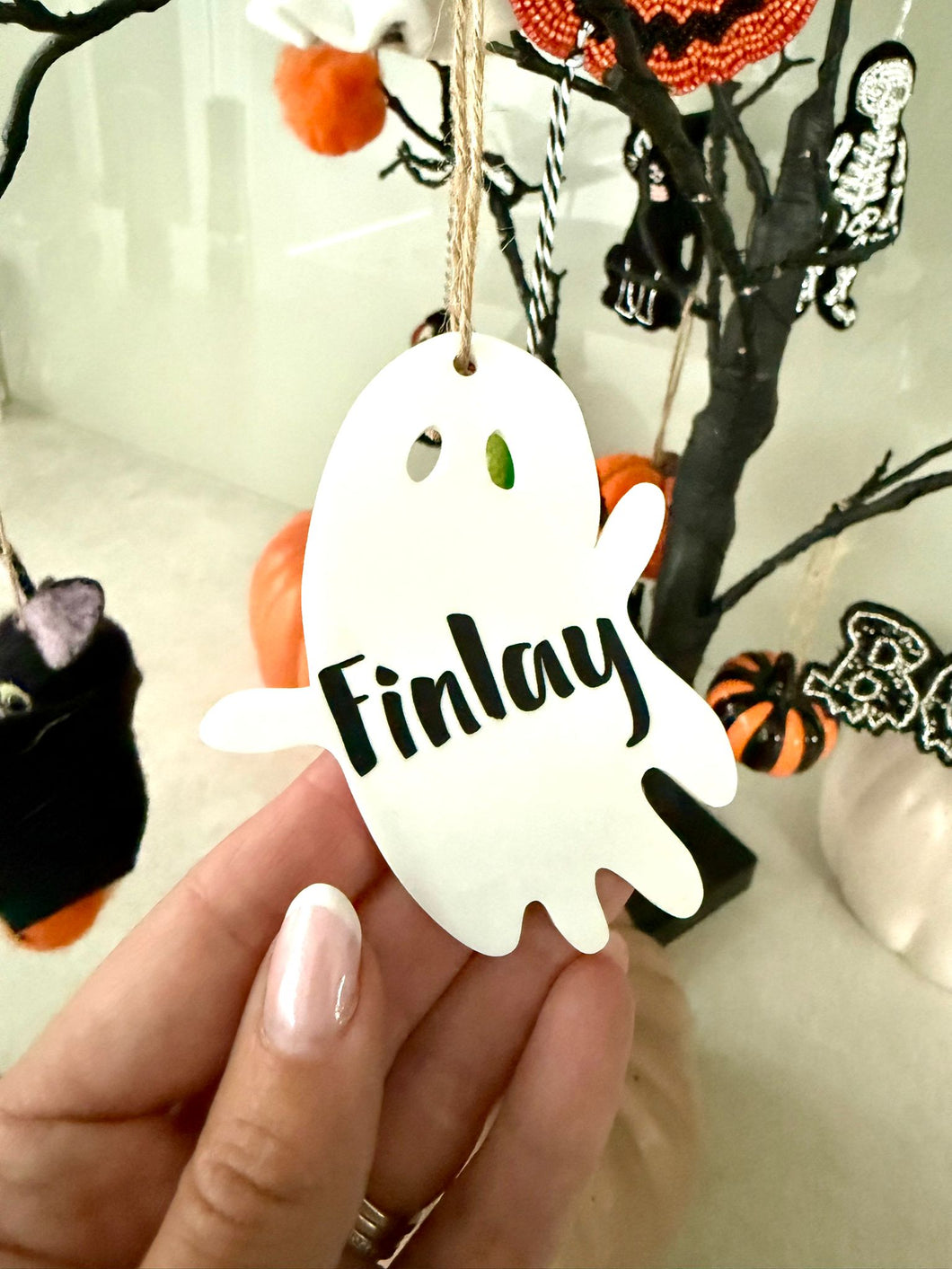 Personalised ghost Halloween tree decoration with engraved name hanging on a Halloween tree with pumpkins and spooky ornaments.