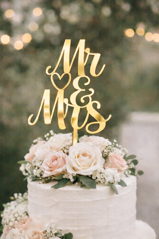 Gold mirror acrylic Mr and Mrs wedding cake topper on a white buttercream wedding cake with blush roses and greenery.
