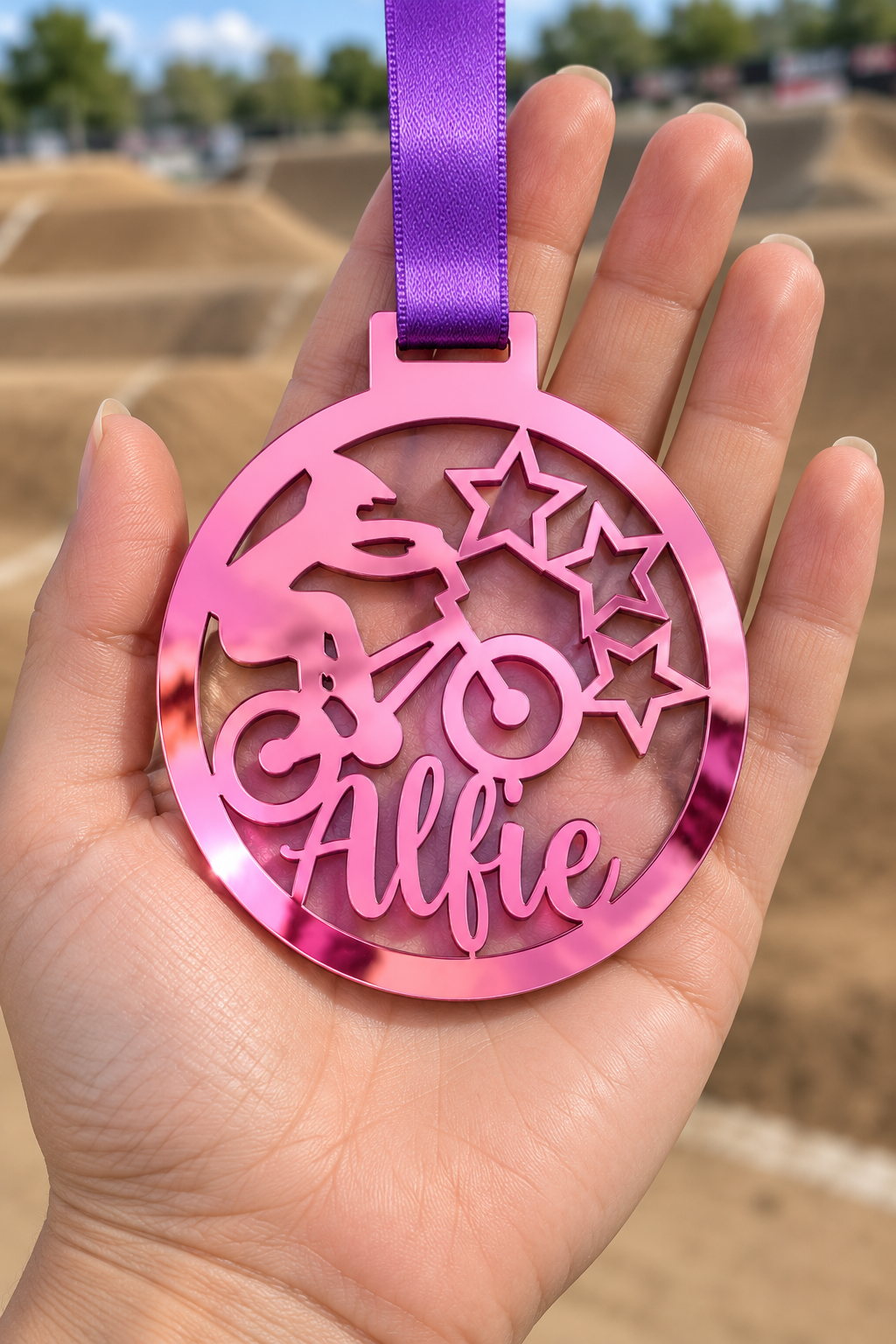 Load image into Gallery viewer, pink mirror acrylic personalised BMX medal with custom name on a purple ribbon, held in hand in front of a blurred BMX track
