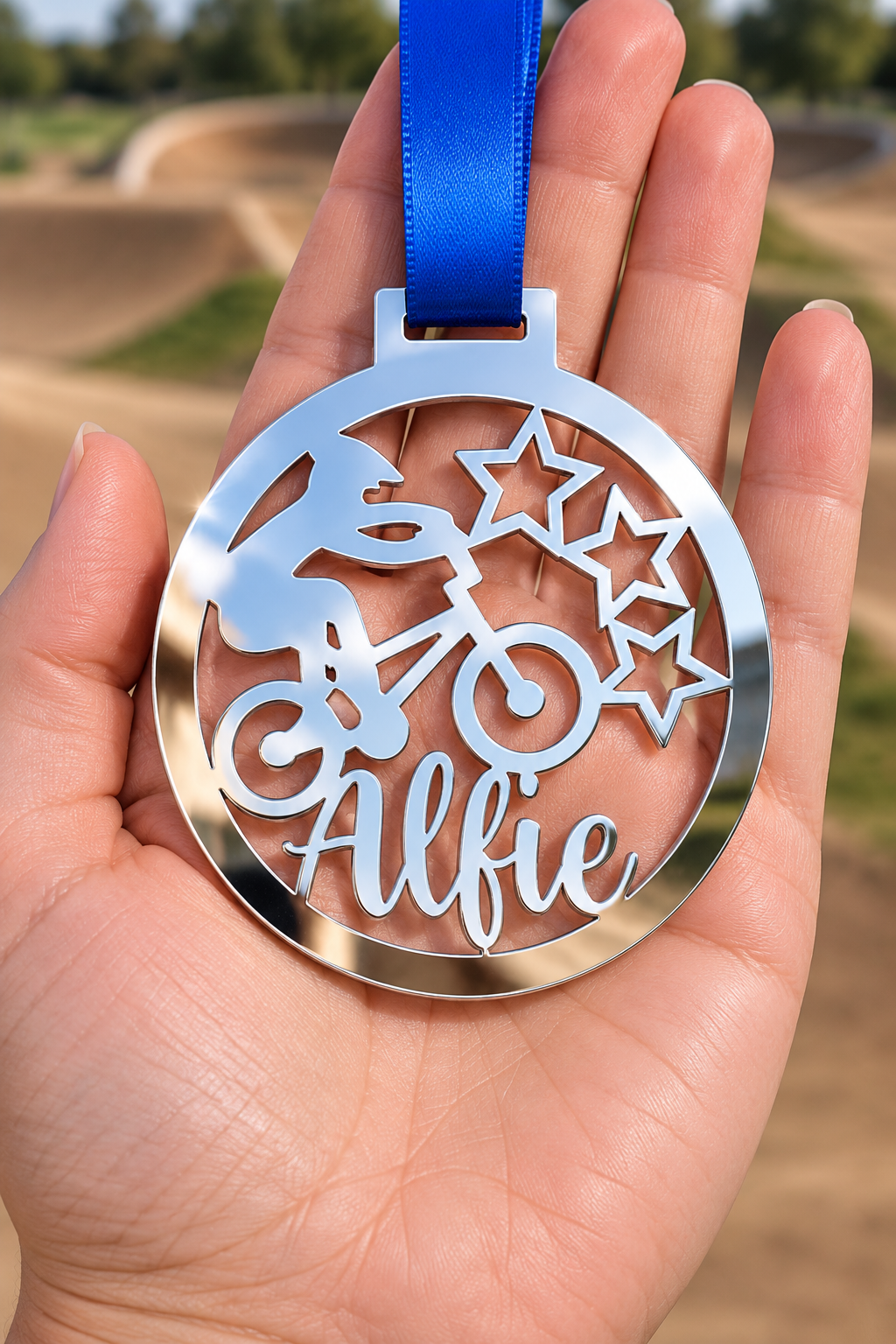 Load image into Gallery viewer, silver mirror acrylic personalised BMX medal with custom name on a blue ribbon, held in hand in front of a blurred BMX track
