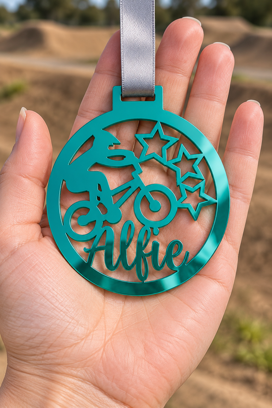 teal mirror acrylic personalised BMX medal with custom name on a silver ribbon, held in hand in front of a blurred BMX track