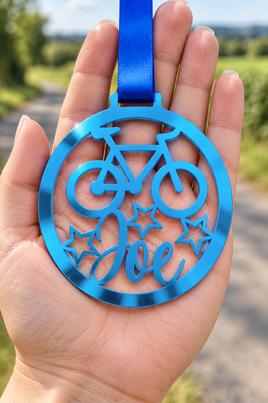 blue mirror acrylic personalised cycling medal with custom name on a blue ribbon, held in hand in front of a blurred country road